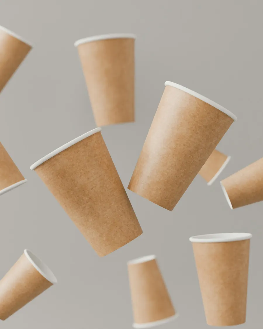 Mehrere Kaffeebecher aus Kraftpapier schweben vor grauem Hintergrund