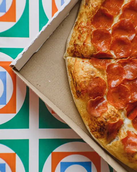 Pizza im offenen Pizzakarton auf gemustertem Untergrund